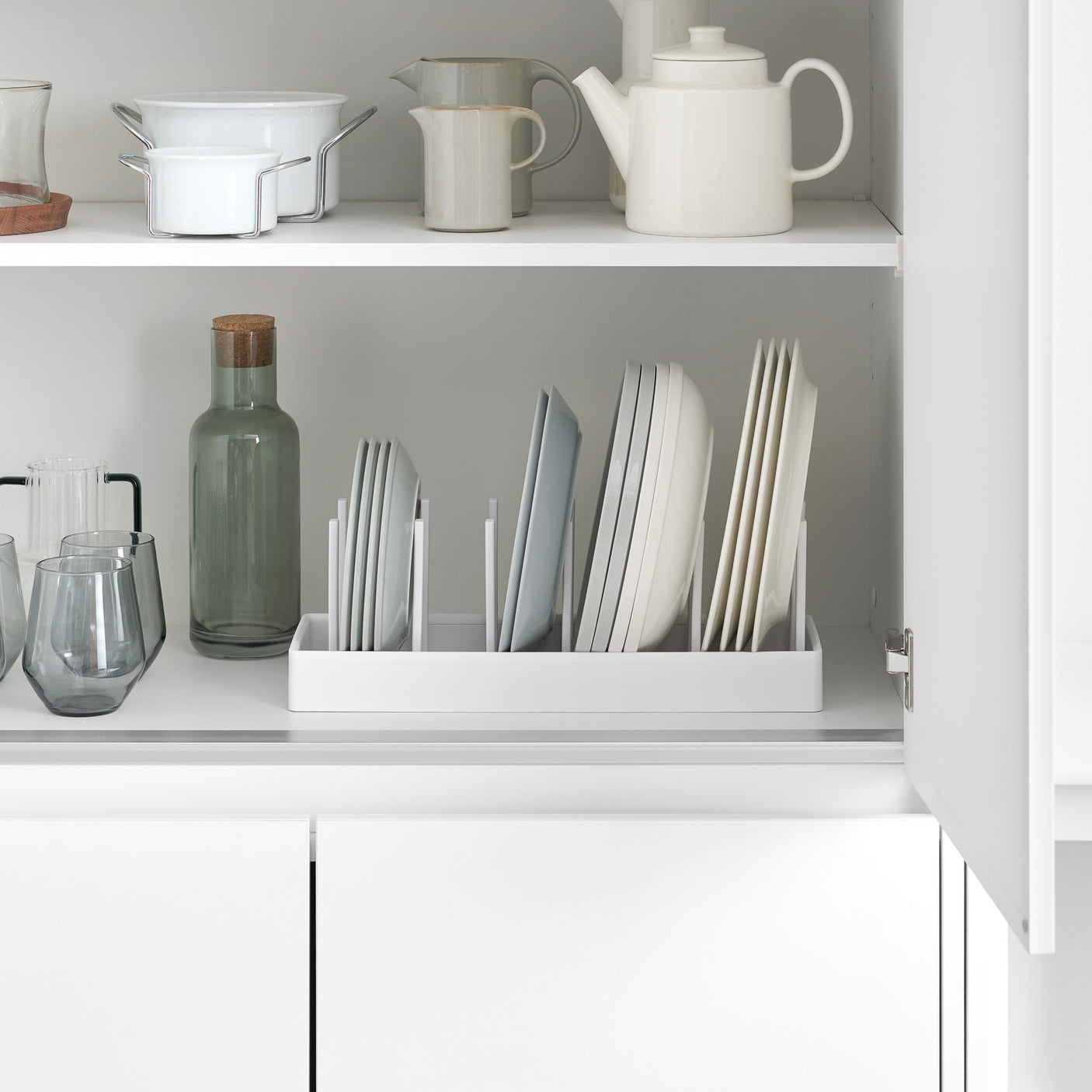 Justerbar gryteholder i hvit plast brukt i kjøkkenskuff med gryter og lokk.