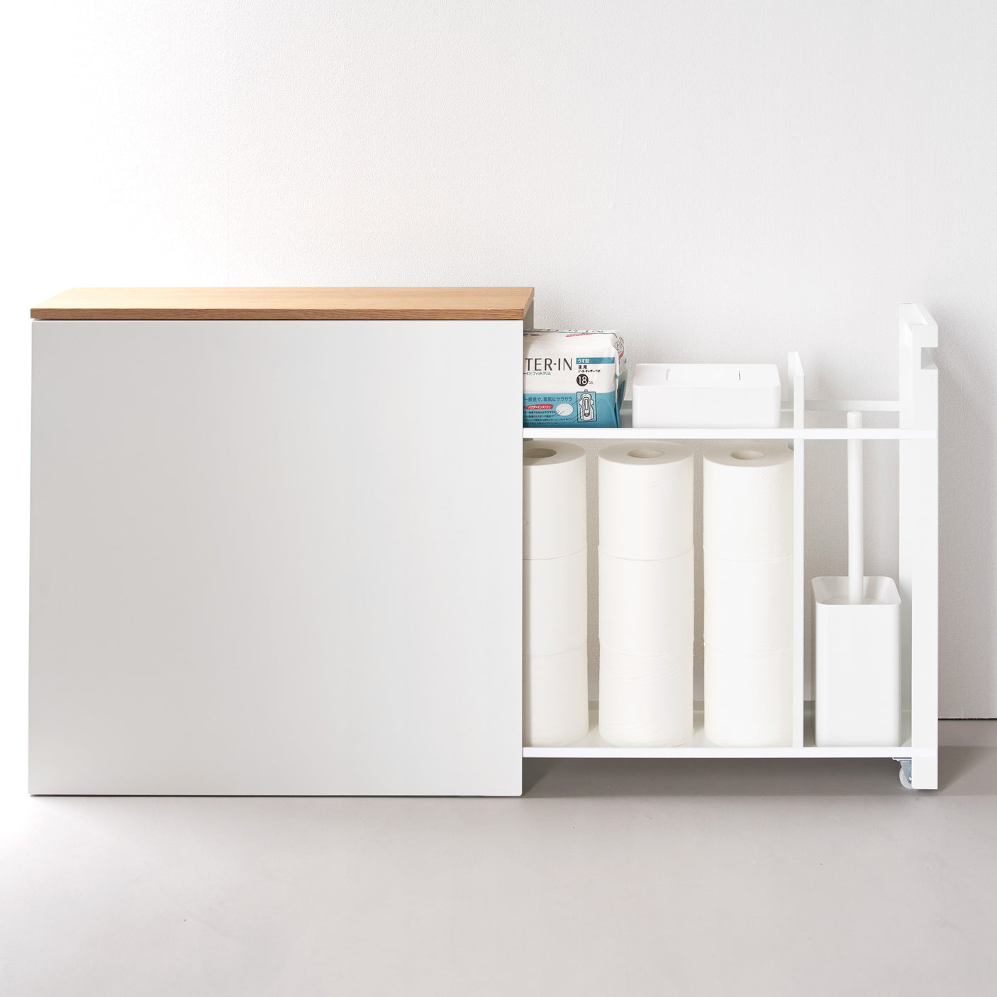 Hvit oppbevaringshylle med skyvbar treplate plassert på baderom med toalett og planter.