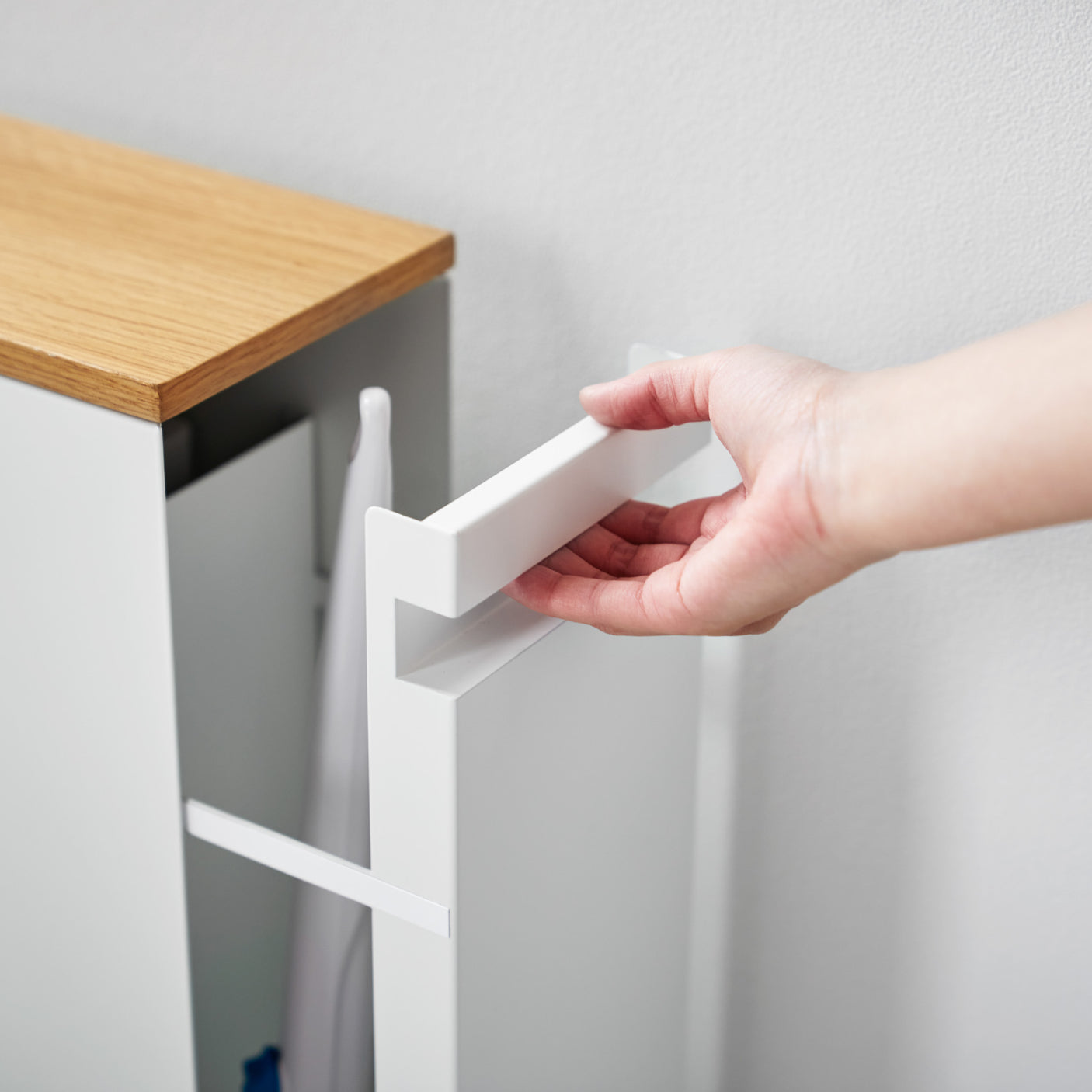 Hvit skyvehylle på hjul med plass til rengjøringsartikler og toalettruller, brukt i moderne bad.