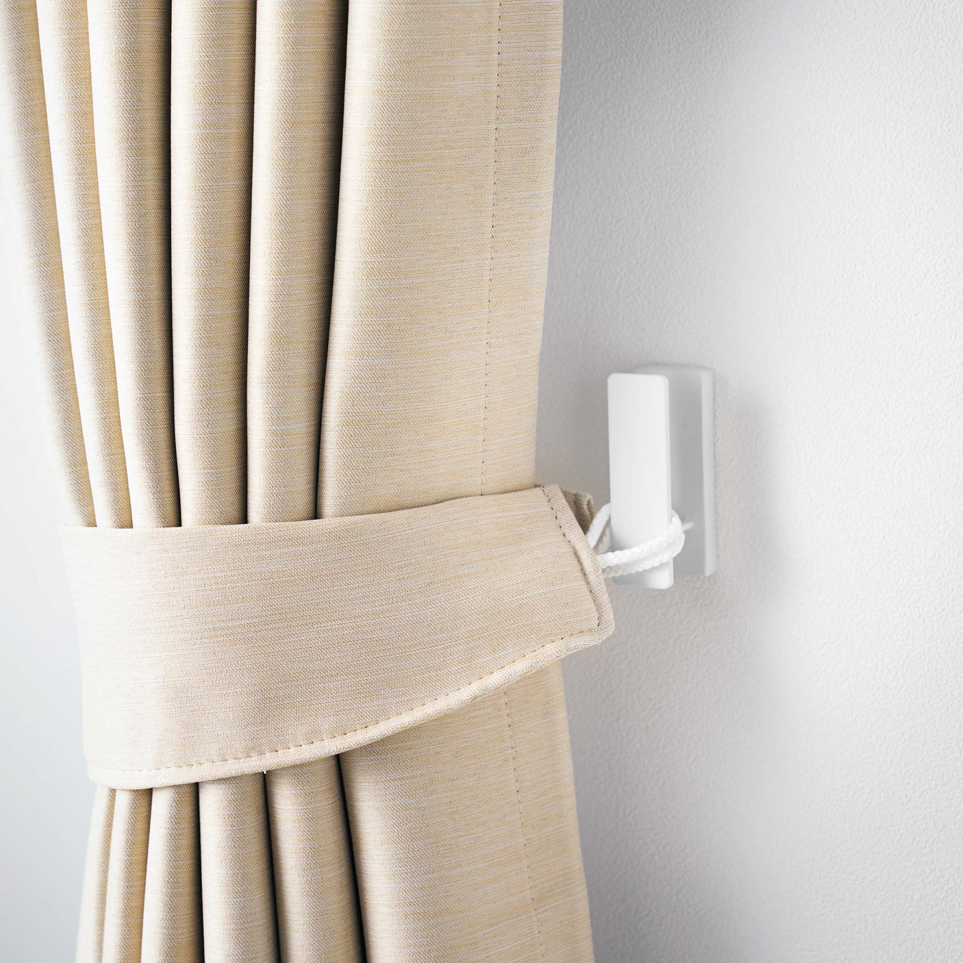 Nærbilde av hvit metallkrok festet med skrue i lys vegg.