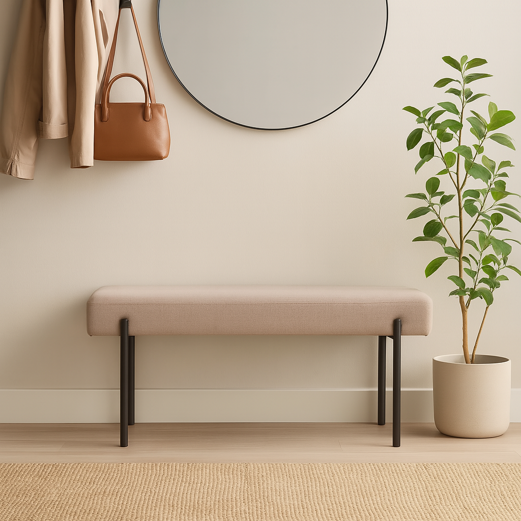 En minimalistisk gang med en beige polstret benk, rundt speil over, grønn plante og lykt på benken, samt krokrekke med jakke og veske.