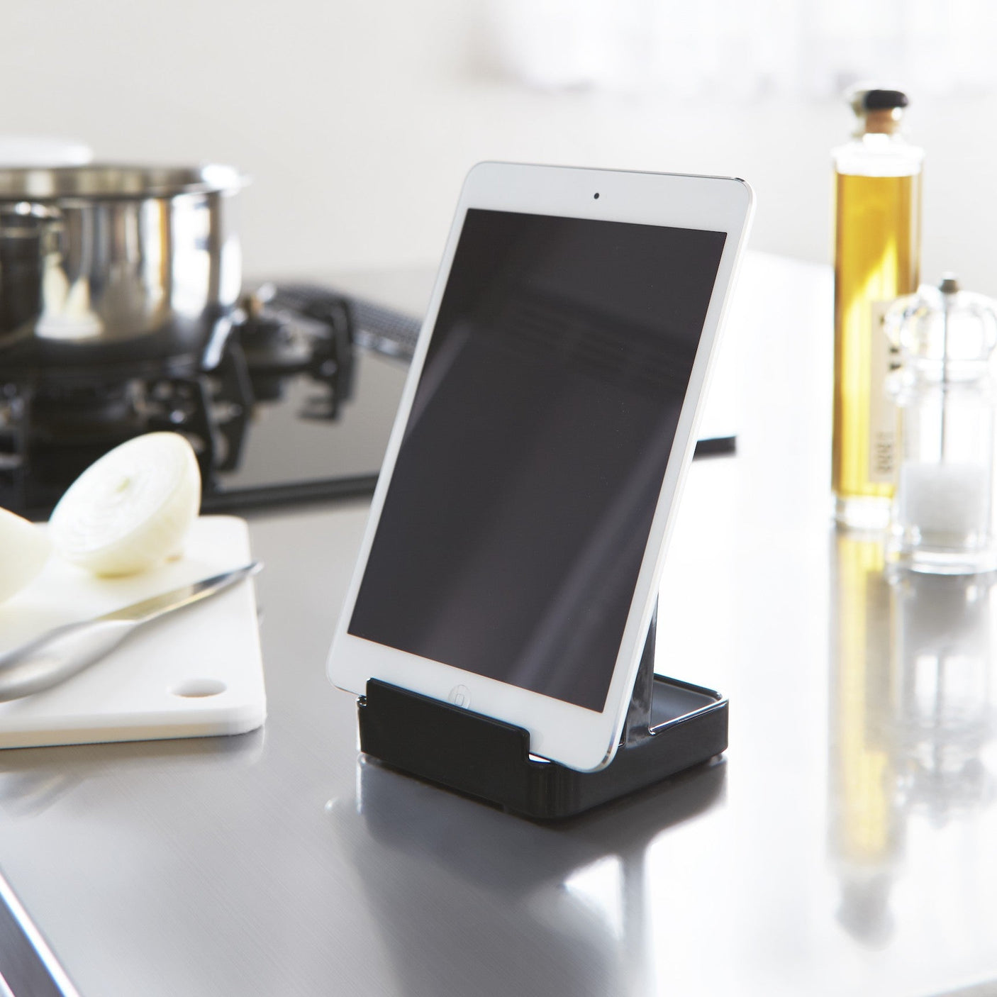 Praktisk sort kjøkkenstativ med sleiver og lokk, plassert ved kokeplate for enkel tilgang.