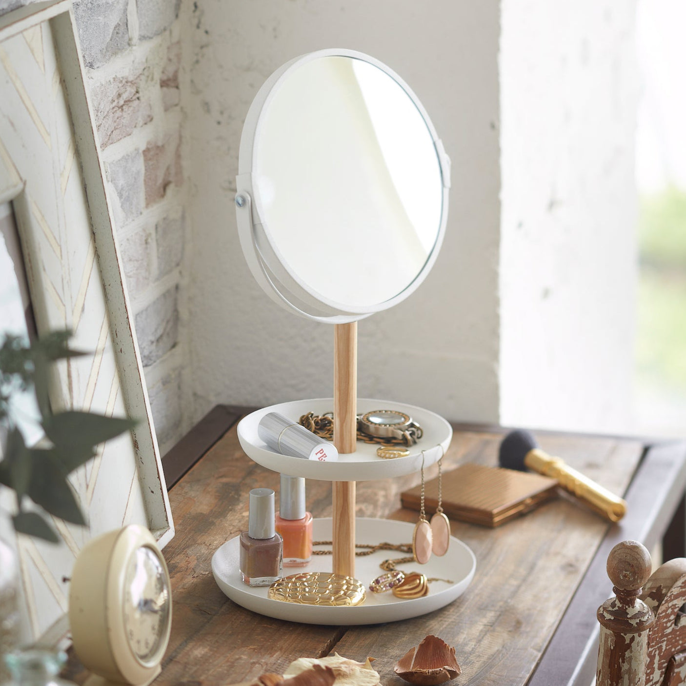 Smykkebrett med speil plassert på et bord med smykker og sminke.