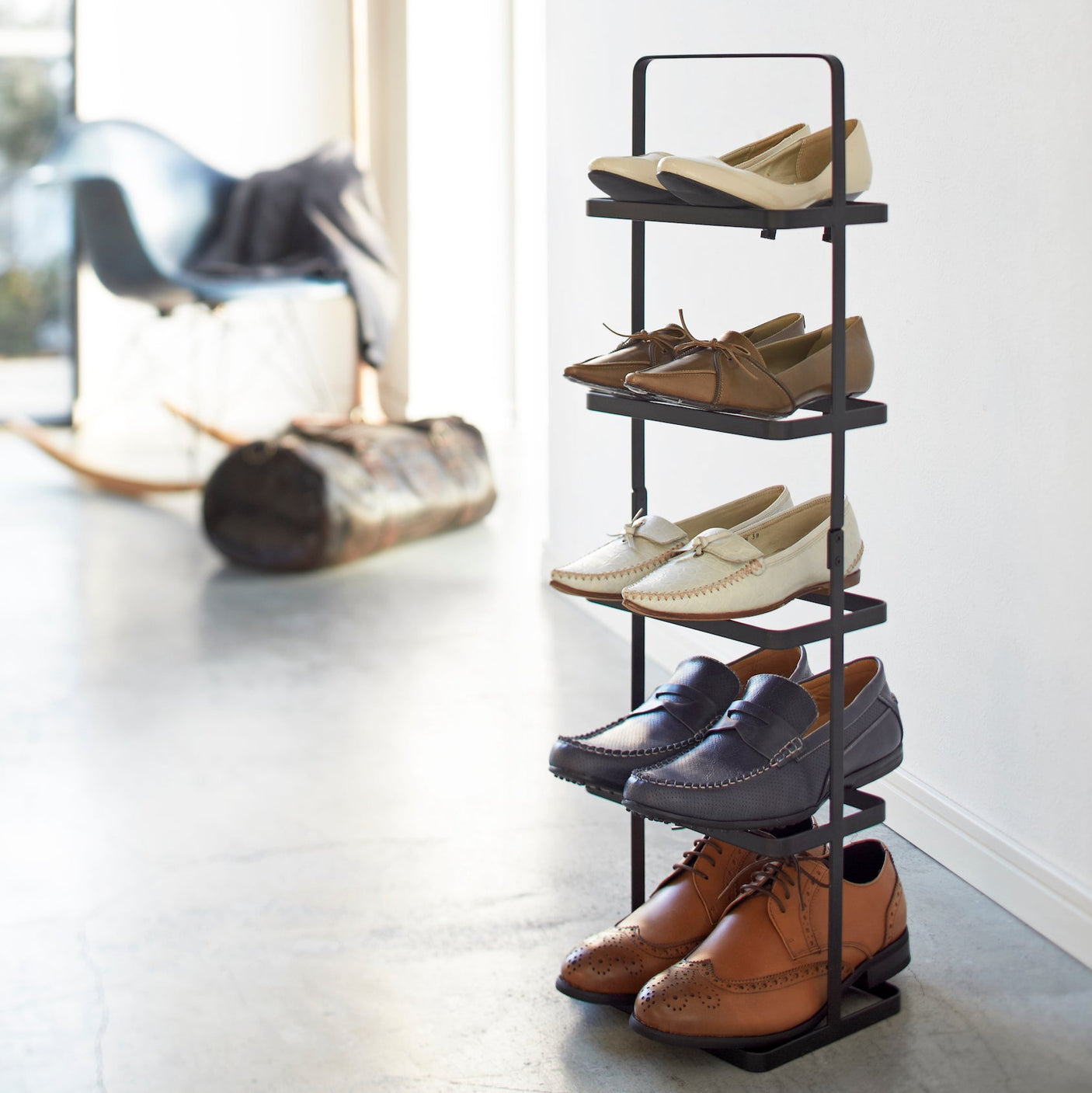 Sort skohylle med fem hyller, plassert mot en lys vegg med flere par sko organisert.