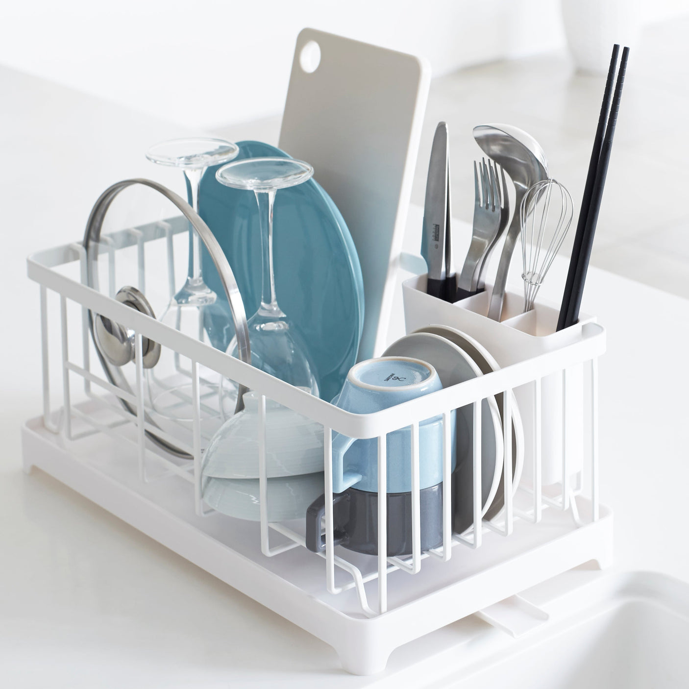 Hvit oppvaskstativ med drypprenne plassert ved vasken, fylt med tallerkener og glass.