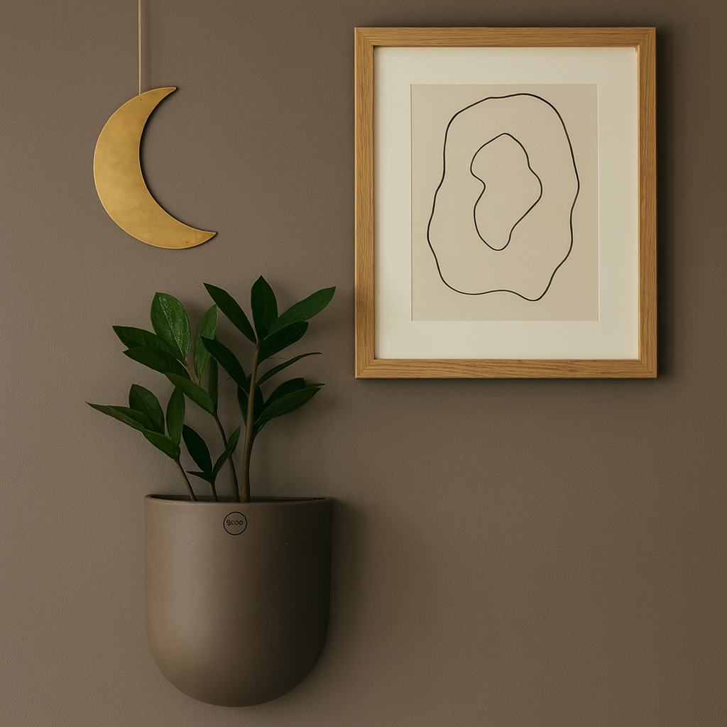 Stor keramikkpotte med plante på brun vegg, stylet med månepynt og innrammet kunst.