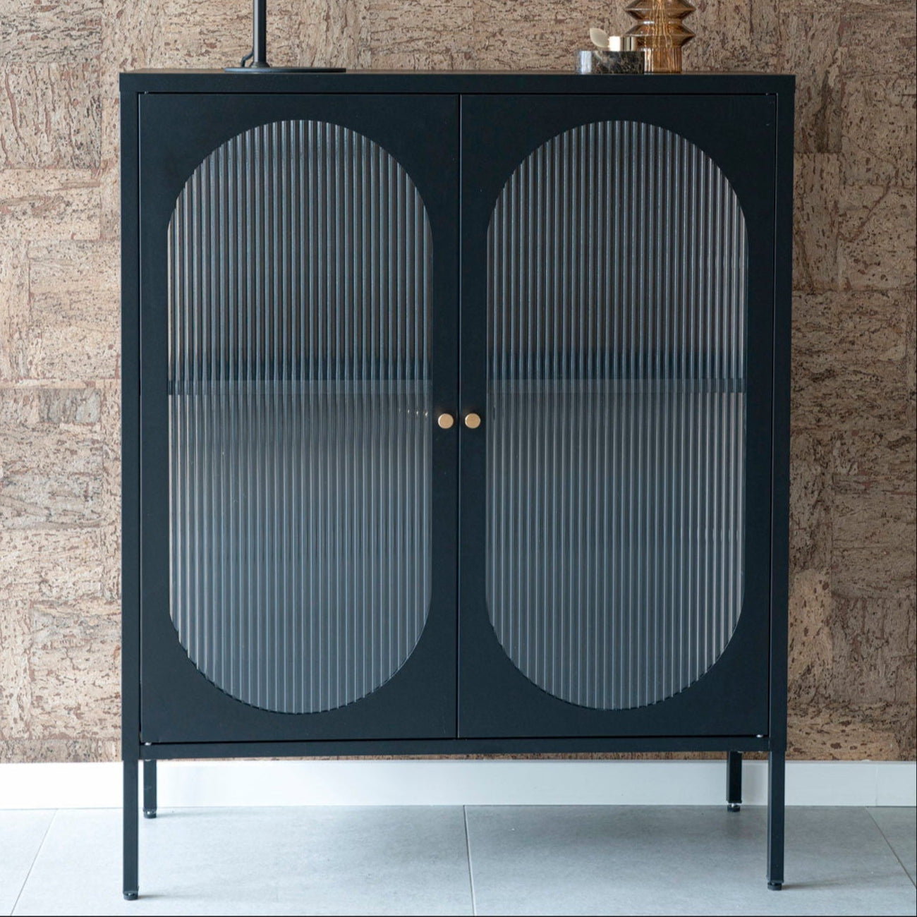 Svart oppbevaringsskap med riflede glassdører og messinghåndtak.