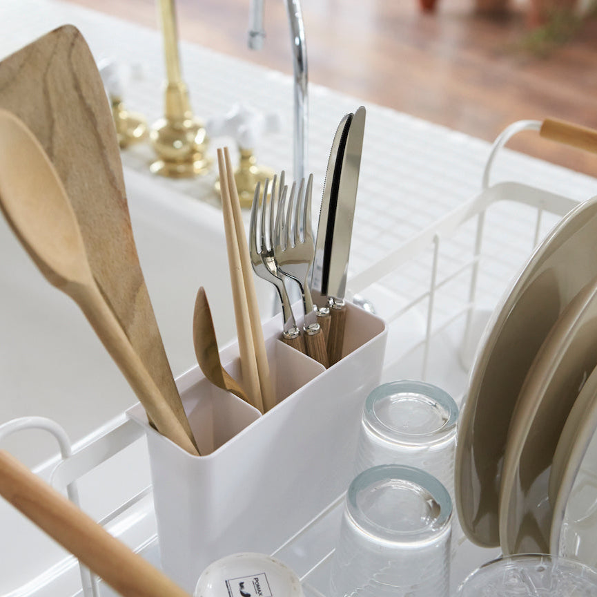 Oppvaskstativ med tallerkener og kopper, plassert på kjøkkenbenk ved vasken.