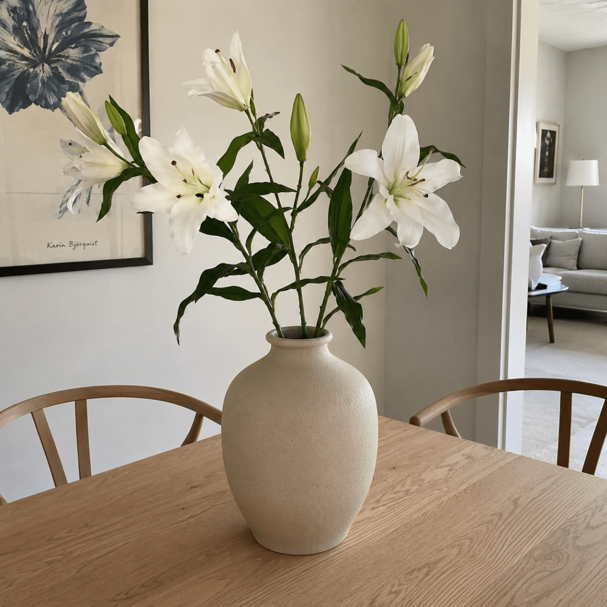 Kunstig vit lilja med realistiska blommor och blad på grön stil. I en kraftig keramikvas i ett nordiskt hem