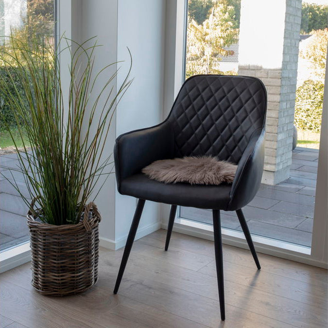 Sitteunderlag i mushroom-farget kunstig saueskinn plassert på stol ved spisebord – nordisk interiør