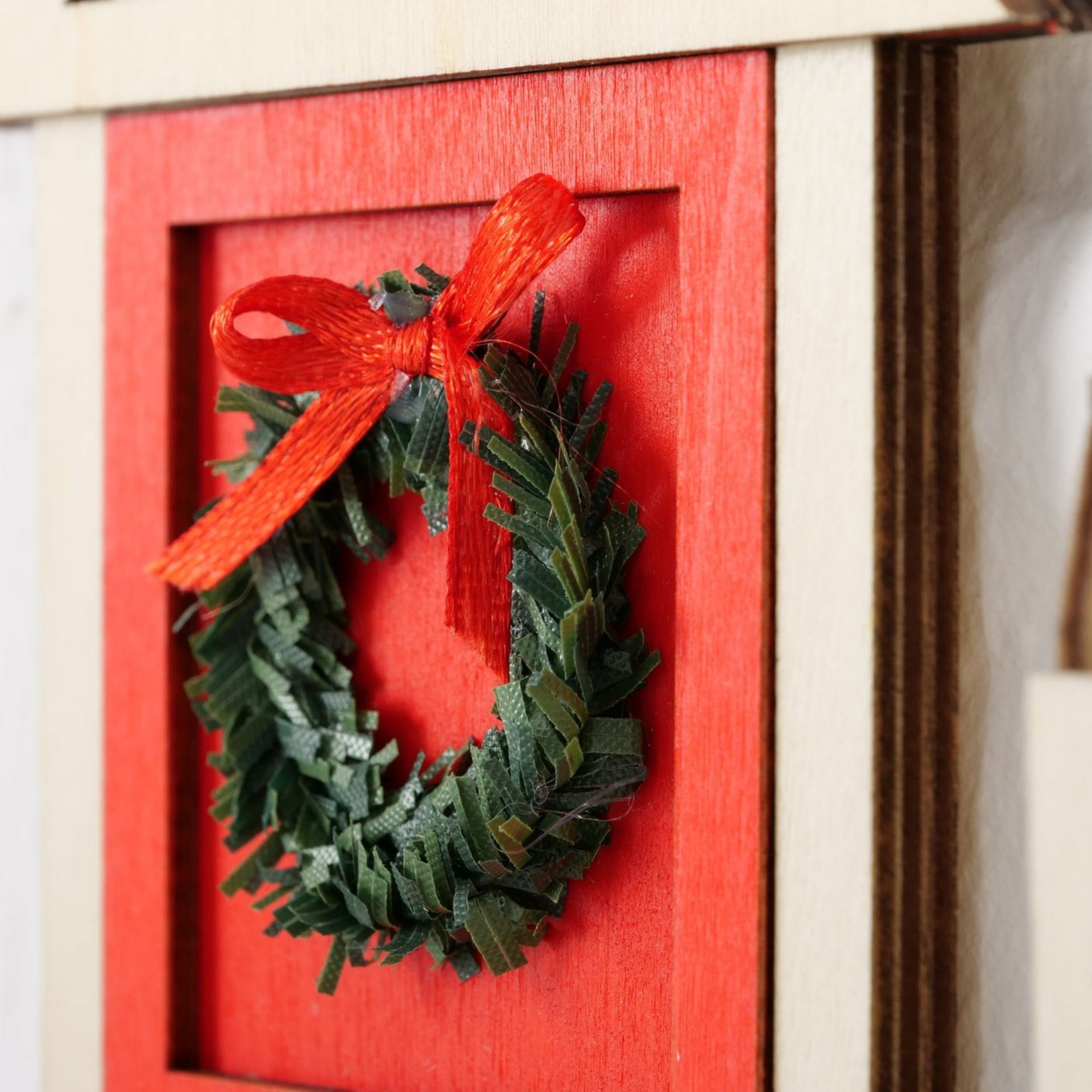 Nærbilde av grønn julekrans med rød sløyfe på rød miniatyrdør.