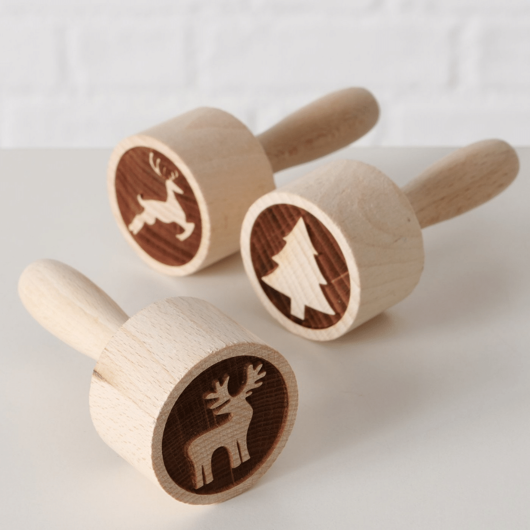 Tre kakestempler i tre med juletre- og elgmotiv, stående og liggende på lys bakgrunn.