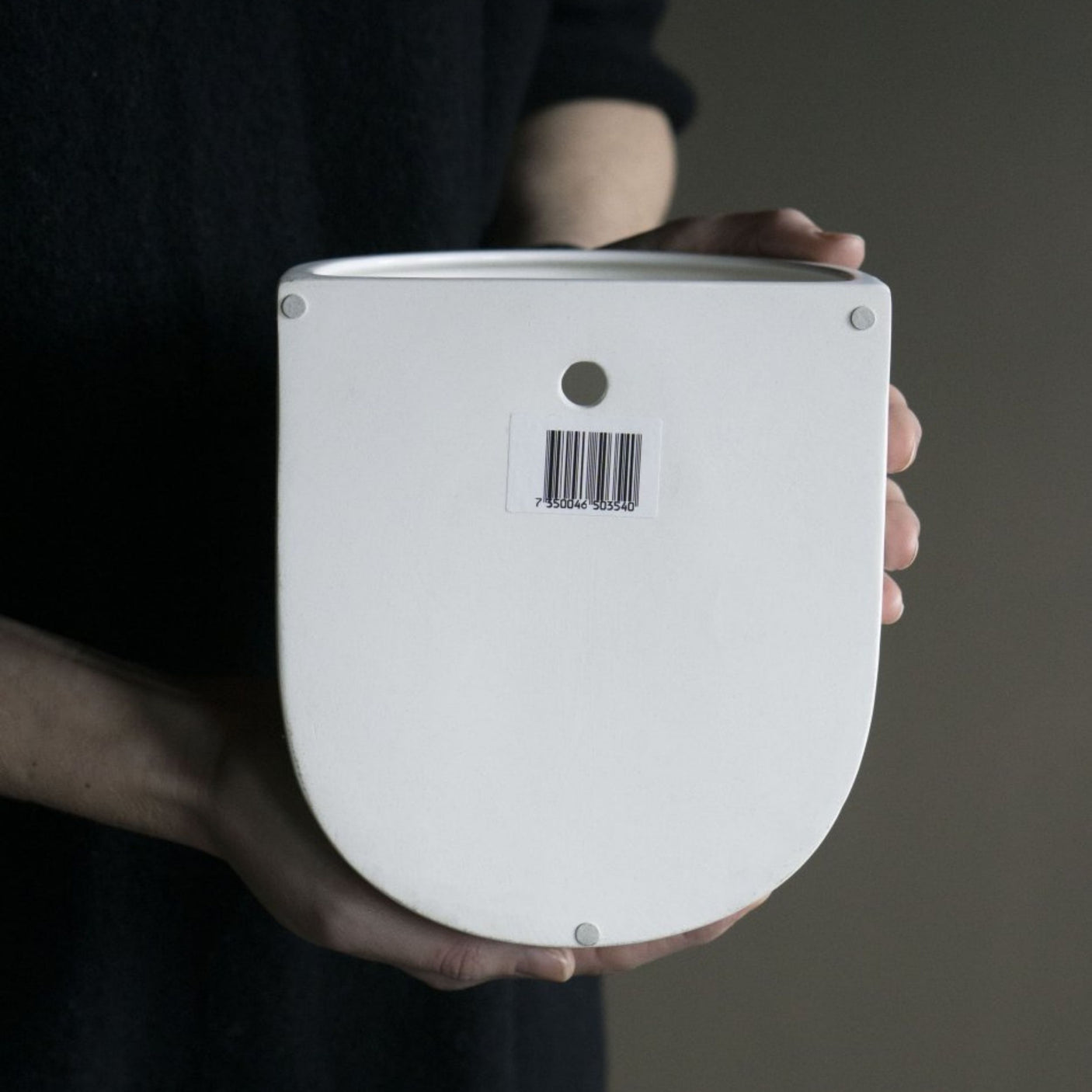 Person holder en veggpotte i keramikk med hull til oppheng og strekkode på baksiden.