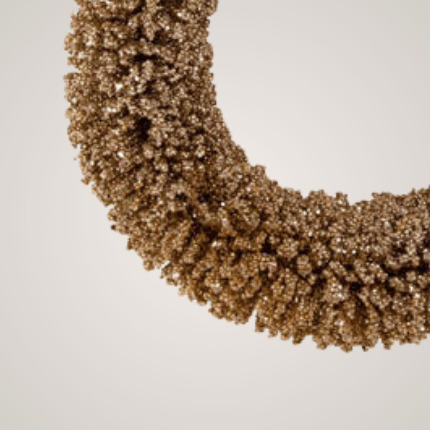 Nærbilde av gullglitrende julekrans som viser tekstur og detaljer på perlene.