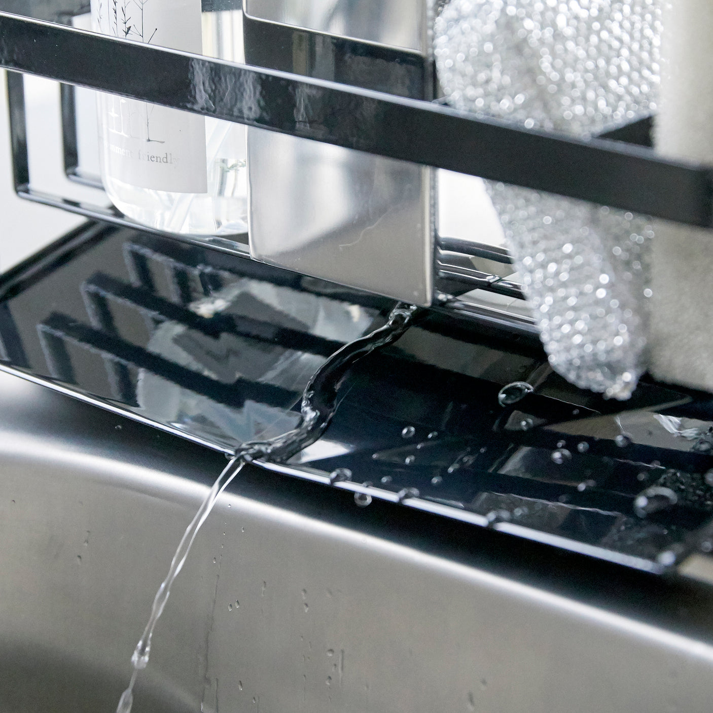 Såpeholder i bruk ved kjøkkenvask som organiserer rengjøringsartikler.