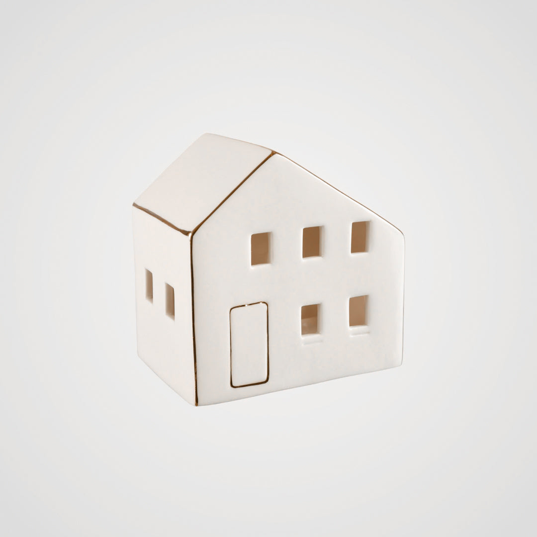 Hvitt keramikkhus med lys inni, plassert på et bord i en koselig stue.