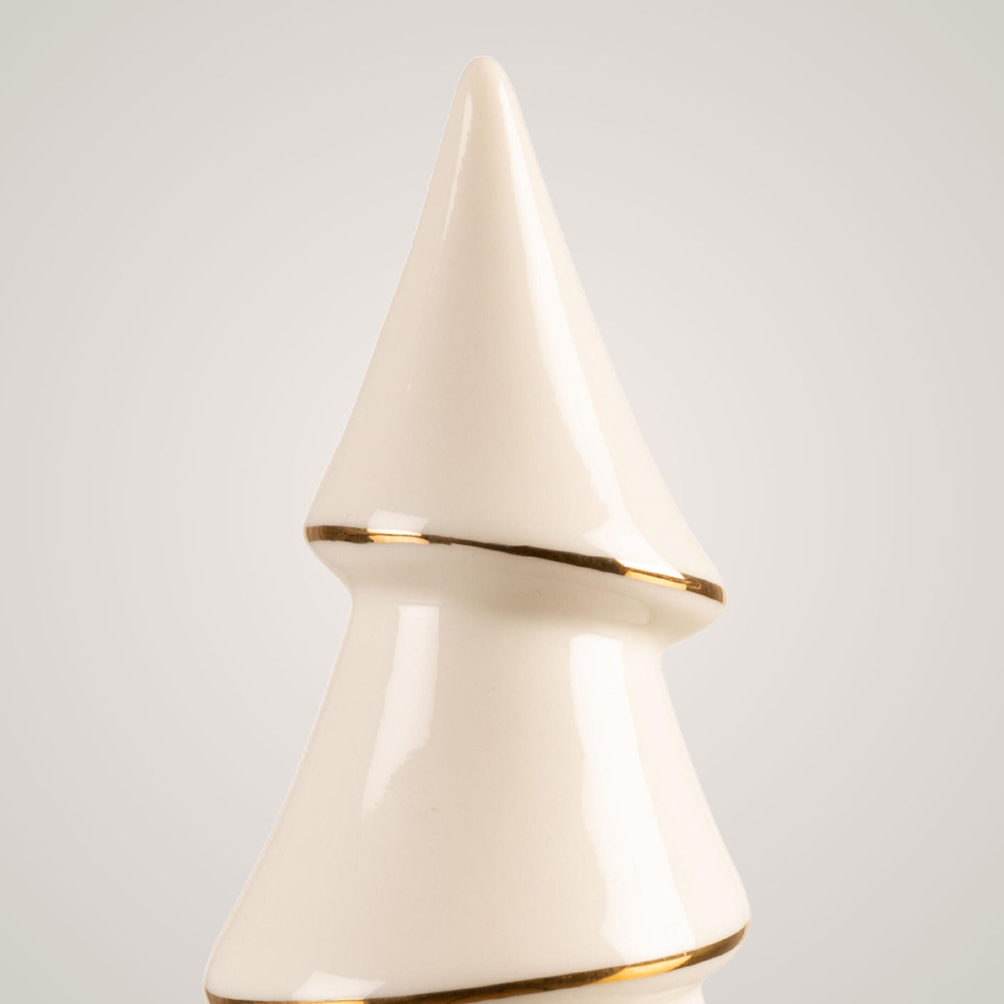 Nærbilde av toppen på kremfarget keramikkjuletre med gullkant.