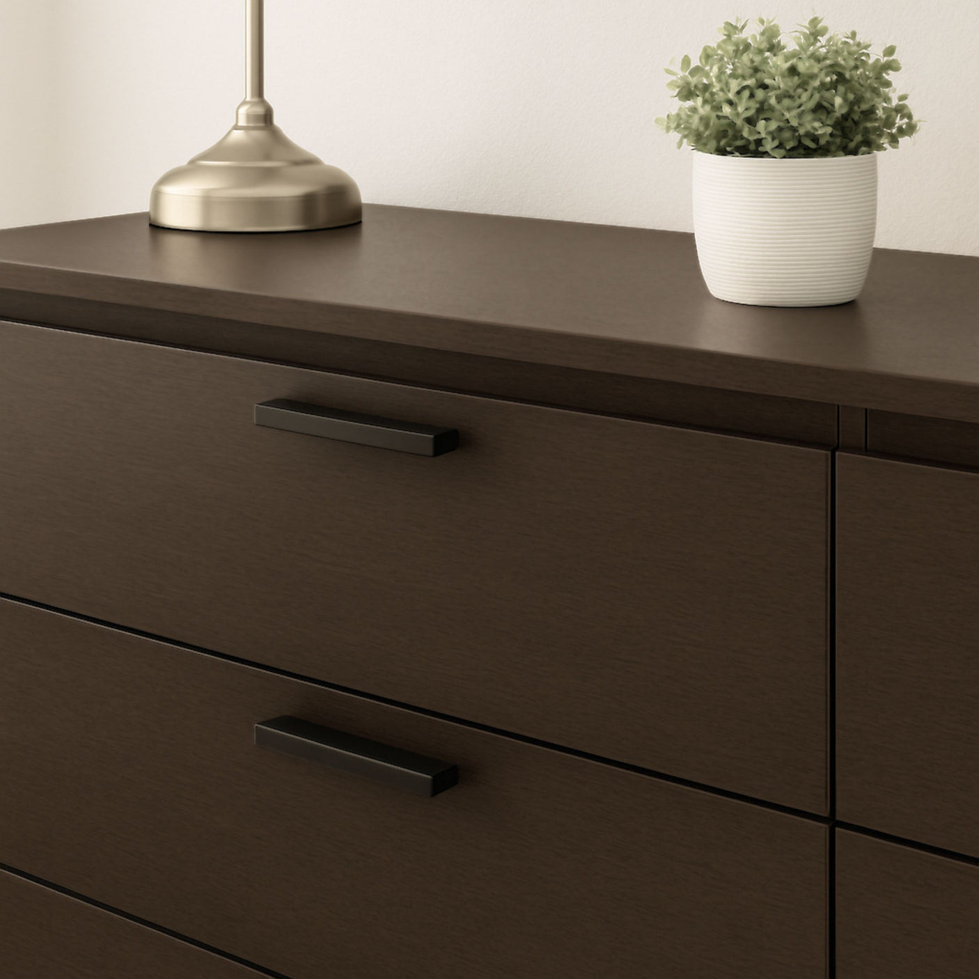 Nærbilde av kommode med Cocoa kontaktplast i mørk trelook, dekorert med gullfarget bordlampe og grønn plante i potte