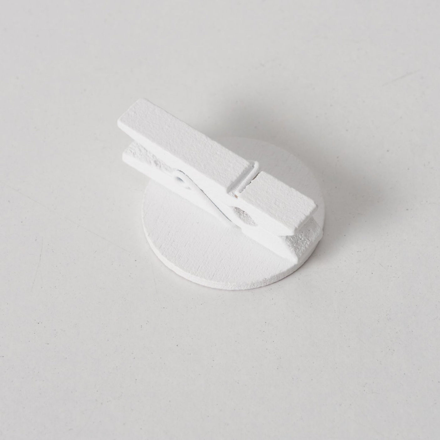 Hvit treklesklype med rund plate på lys bakgrunn.