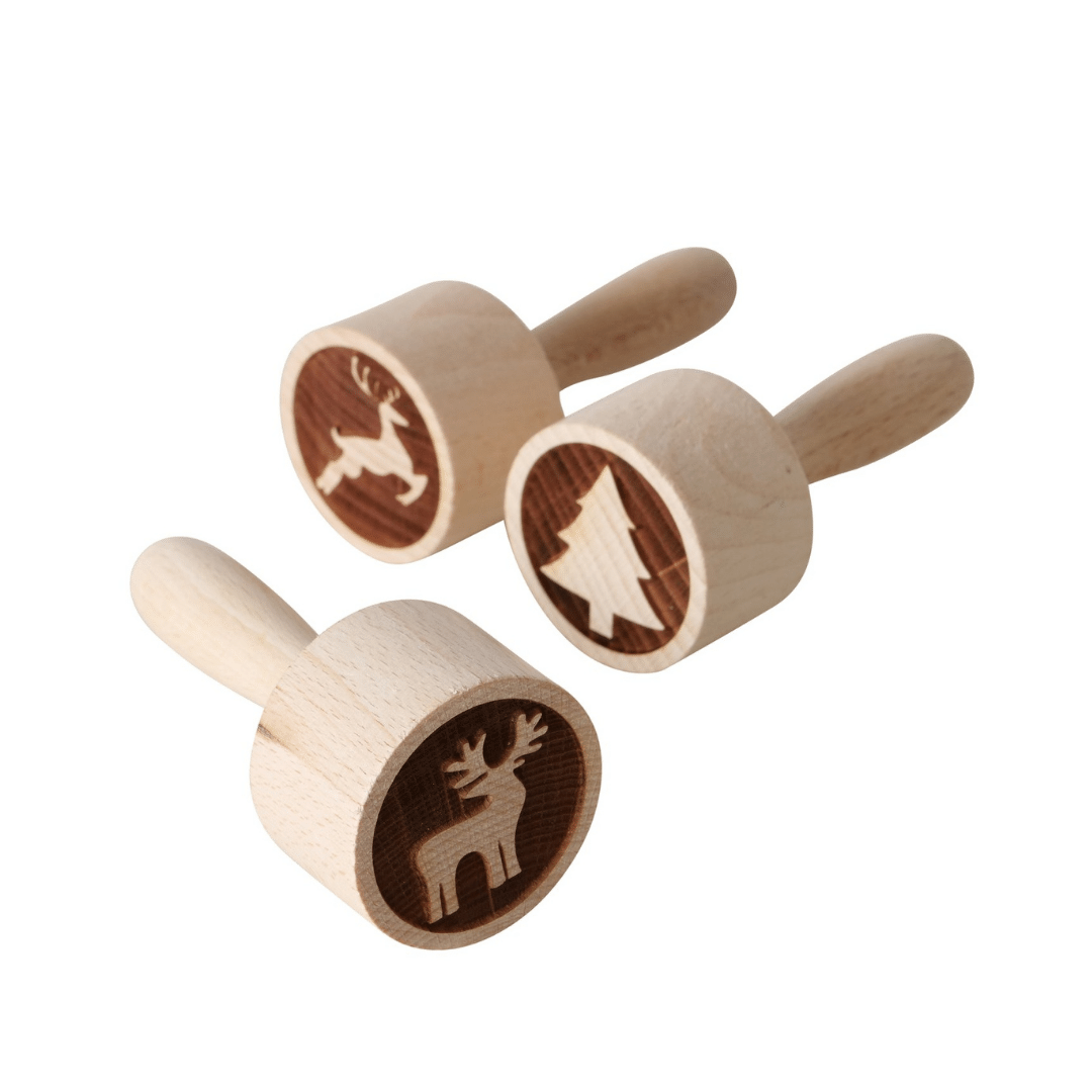 Tre kakestempler i tre med reinsdyr-, juletre- og elgmotiv, liggende på lys overflate.