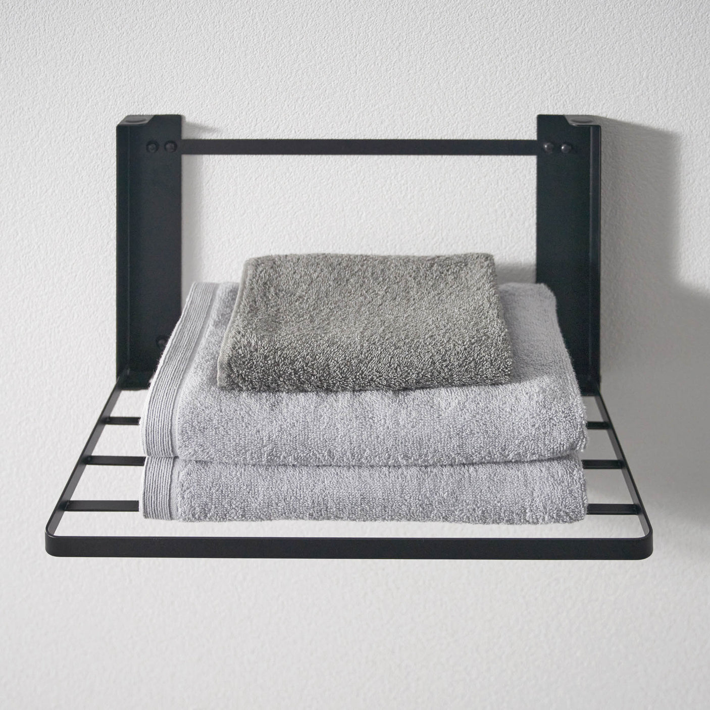 Vegghengt hylle i sort metall for håndklær og oppbevaring.