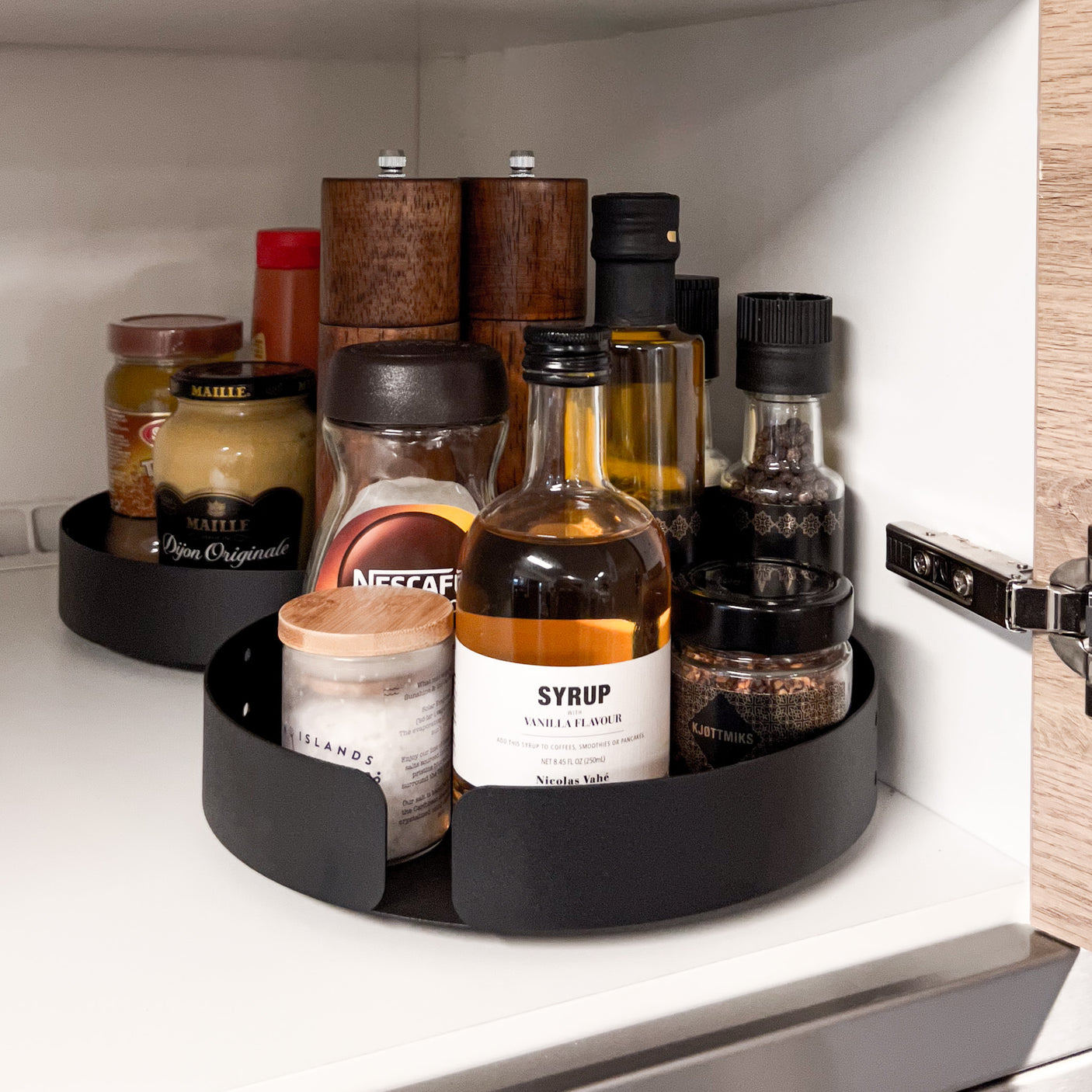 Sort roterende brett med høy kant holder glass og flasker organisert og tilgjengelig – smart løsning for effektiv oppbevaring i kjøkkenskap.