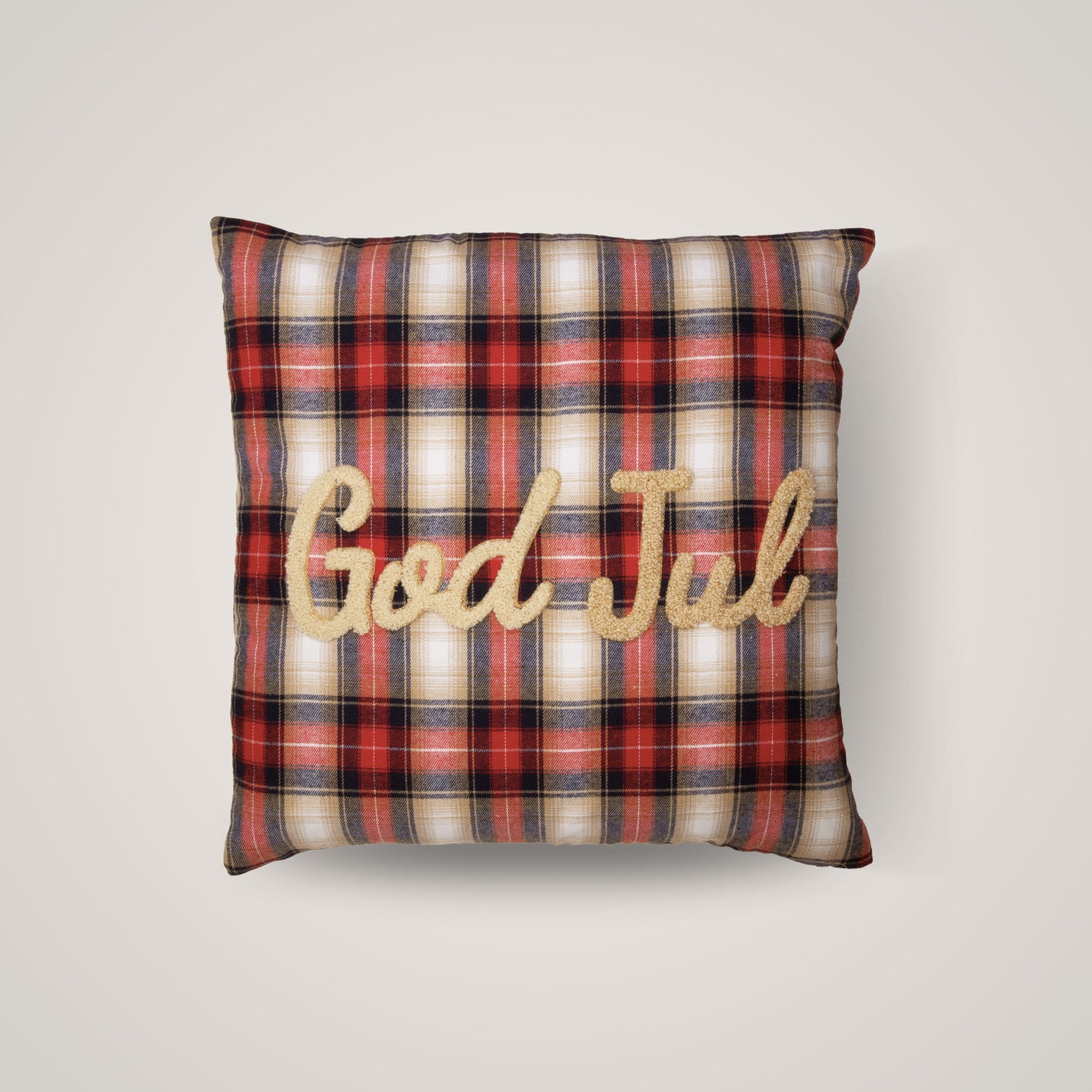 Rødrutete julepute med teksten "God Jul" brodert i gull på lys bakgrunn.