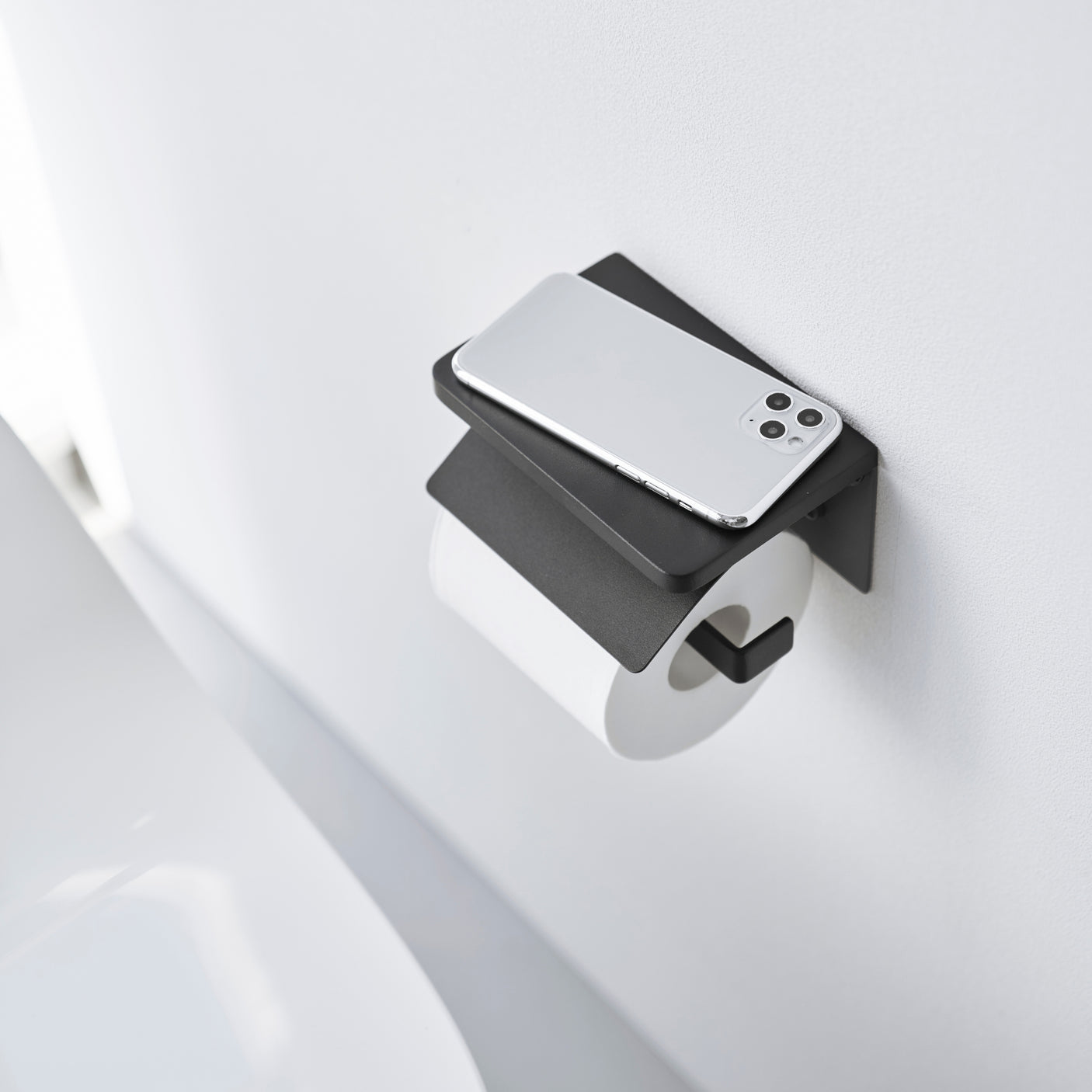 Moderne toalettpapirholder i sort metall med plass til duftpinner og telefon – veggmontert modell.