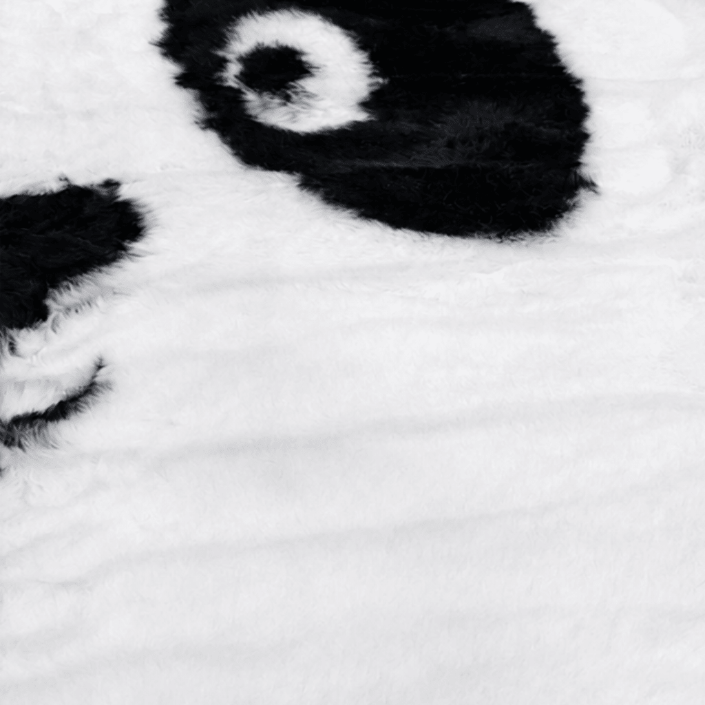 Nærbilde av mykt pandateppe i svart og hvitt med fluffy overflate i polyester, designet som et pandaansikt til barnerom.