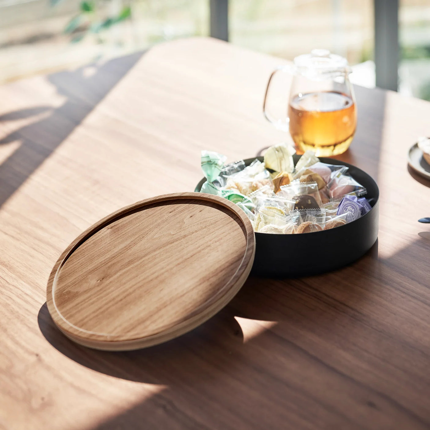 Rund oppbevaringsboks i sort stål med trelokk på lys bakgrunn