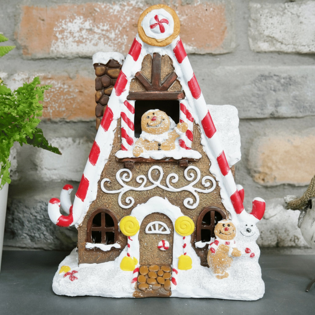 Pepperkakehus med juledekor mot mursteinsbakgrunn, pyntet med sukkerrør, glasur og pepperkakefigurer.