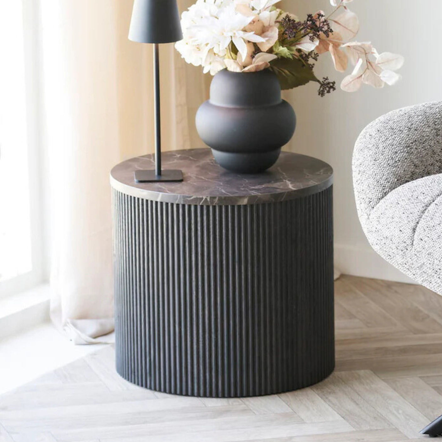 Rundt sofabord i mørk brun marmorlook med riflede sider, dekorert med vase og blomster – elegant og moderne bord til stue.
