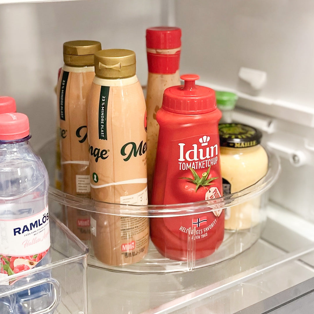 Gjennomsiktig snurrebrett fylt med flasker og glass på benk