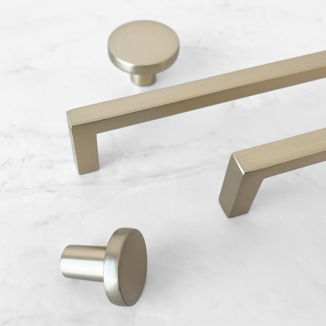 Metallisk håndtak med rette linjer og matt finish i gullaktig tone.