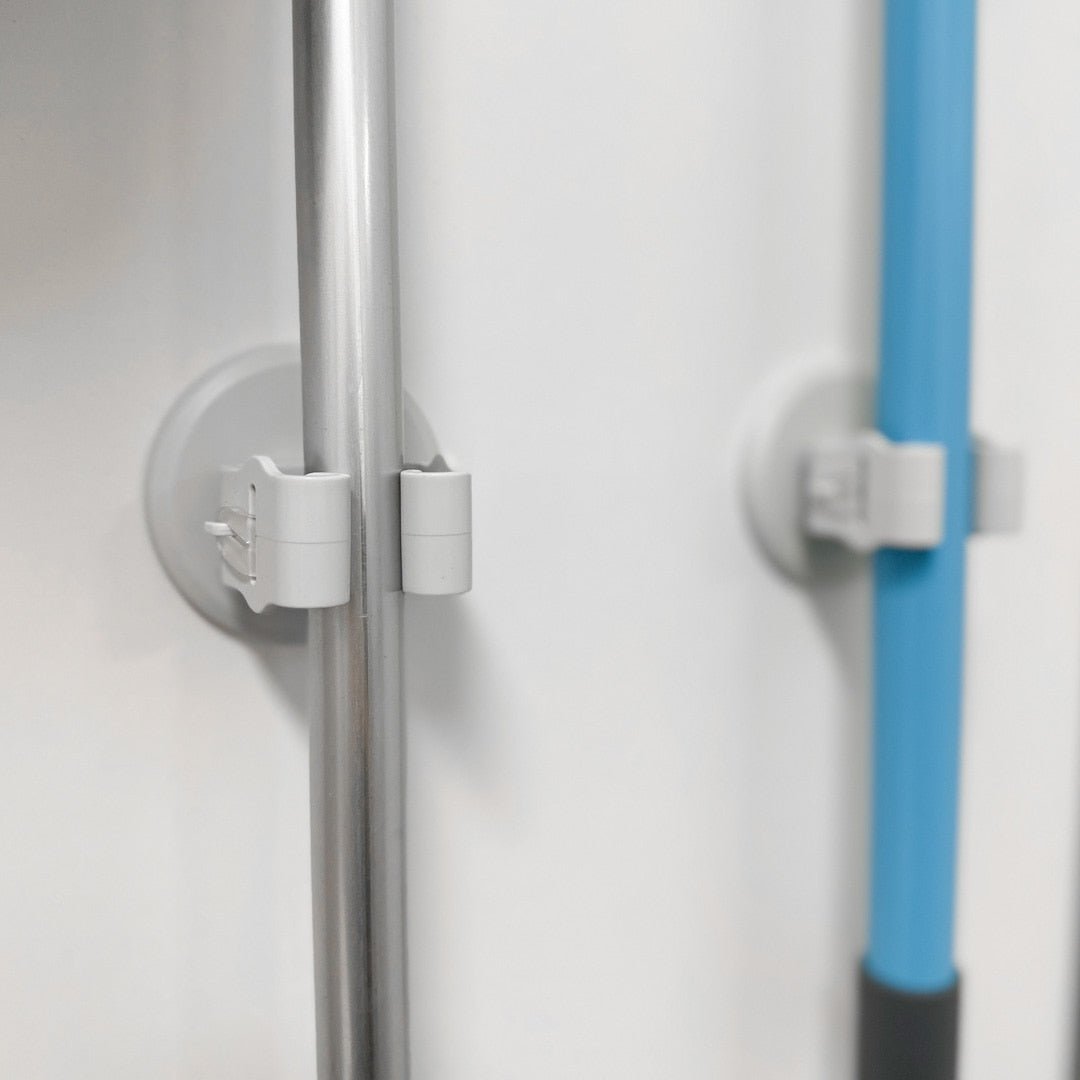 To moppeholdere montert pÄ vegg som holder kosteskaft i metall og plast.