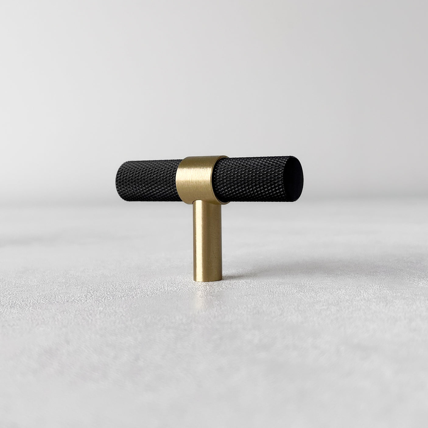 Ett sort og messingfarget T-bar håndtak plassert på lys overflate.