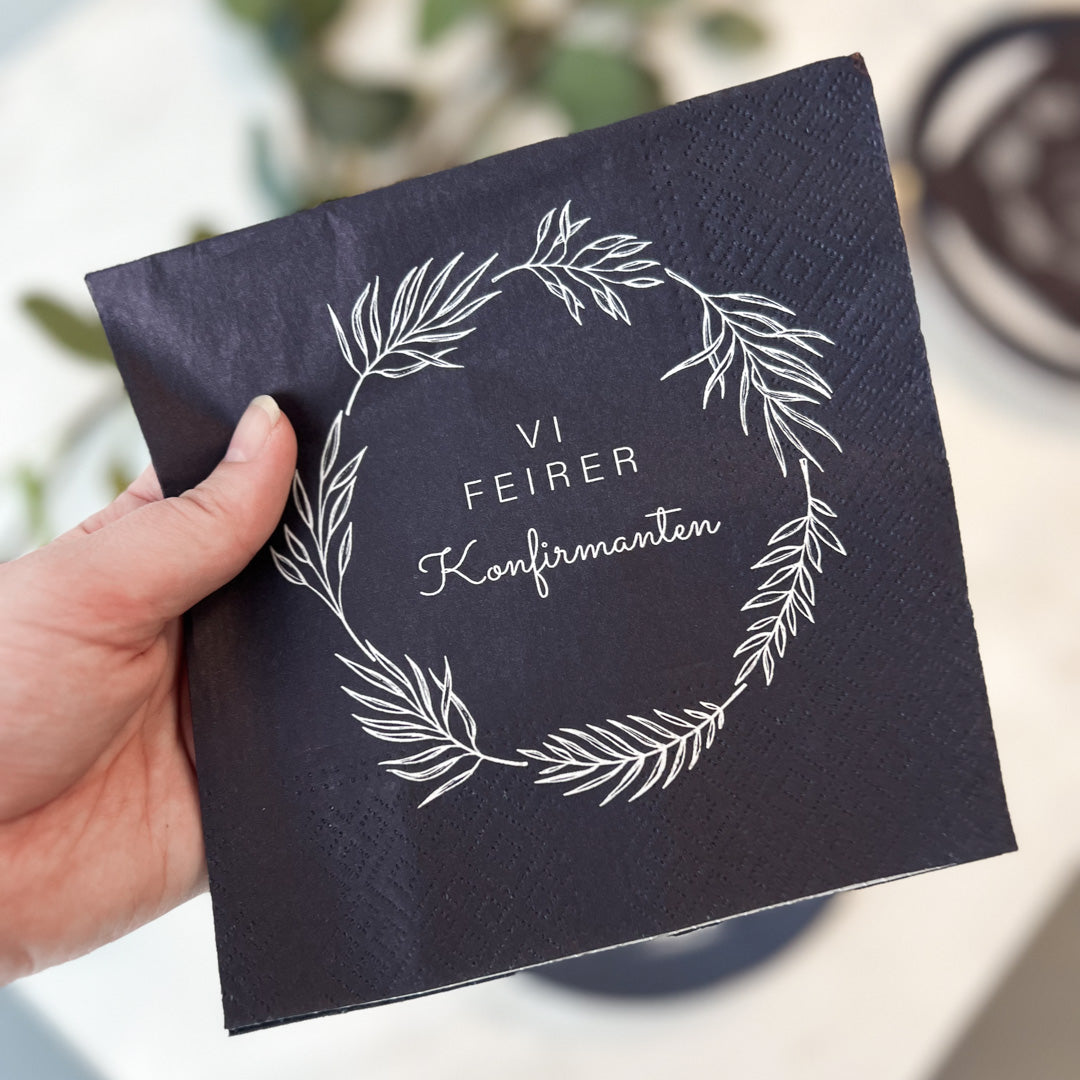 Hånd som holder mørkeblå serviett med teksten «Vi feirer konfirmanten».