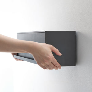 Person åpner sort veggboks for å legge inn småting.