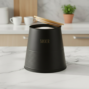 Kvadratisk bilde av sort sukkerboks i metall med åpent bambuslokk på lys kjøkkenbenk