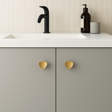 Cannes knott i børstet messing, 36 mm, montert på grått servantskap med hvit benkeplate og sort armatur.

