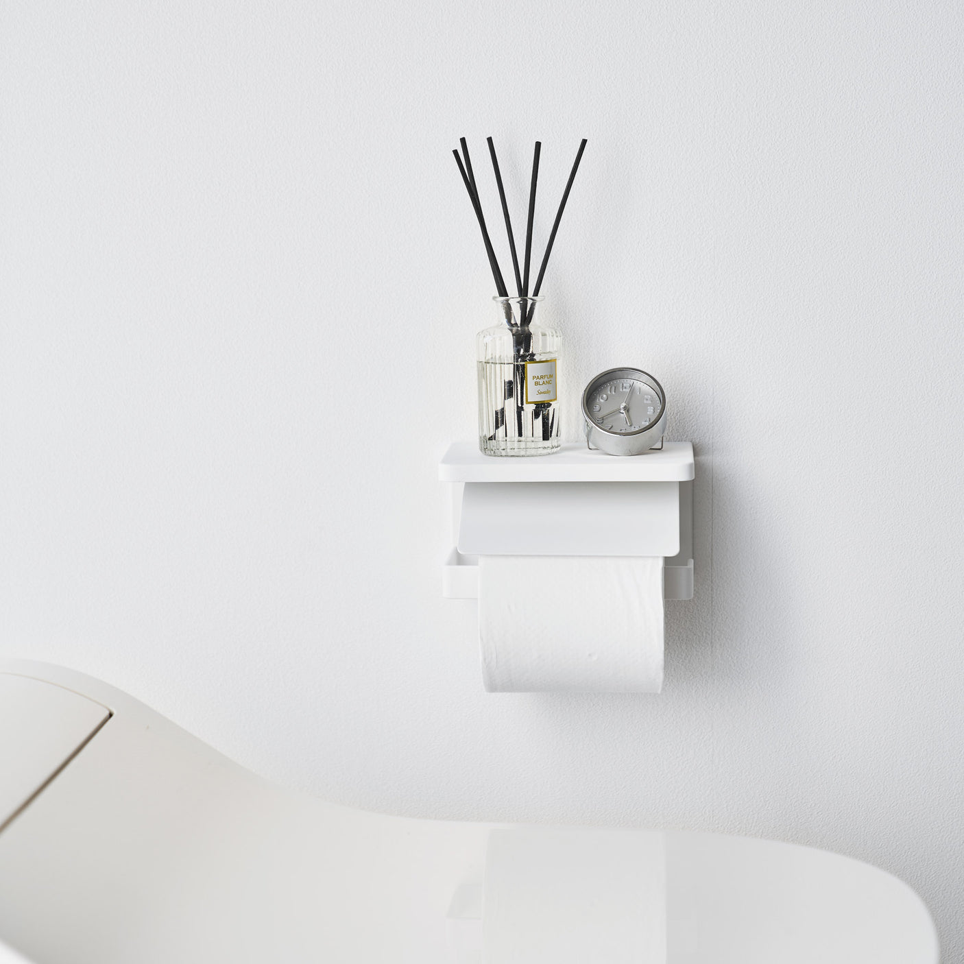 Hvit metallholder for toalettpapir, veggmontert modell med enkel åpning på siden.