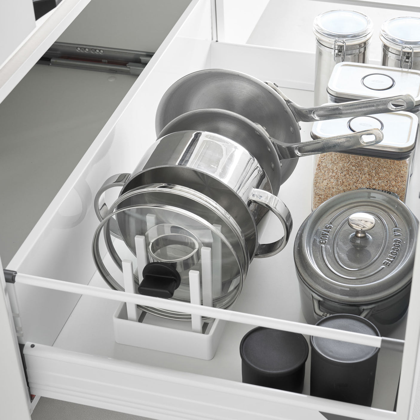 Hvit oppbevaringsholder for gryter, lokk og stekepanner i skuff.