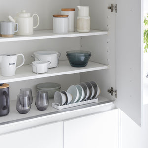 Hvitt skålstativ med sju spor, plassert i kjøkkenskap med hvite tallerkener.