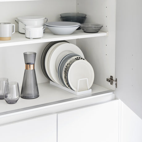 Hvitt tallerkenstativ med oppreist lagring, plassert i skap med servise.