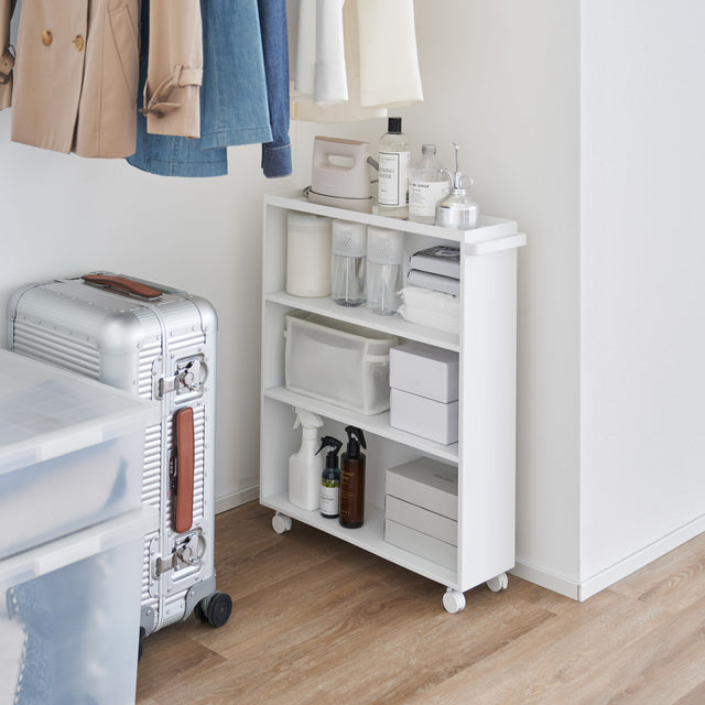 Hvit oppbevaringsvogn på hjul plassert ved seng på soverom.