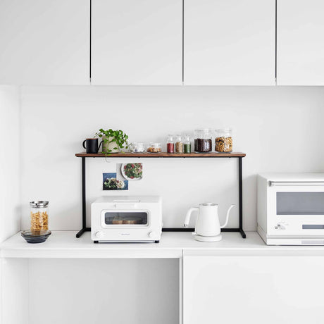 Kjøkkenhylle med krydderglass og planter plassert over kjøkkenapparater