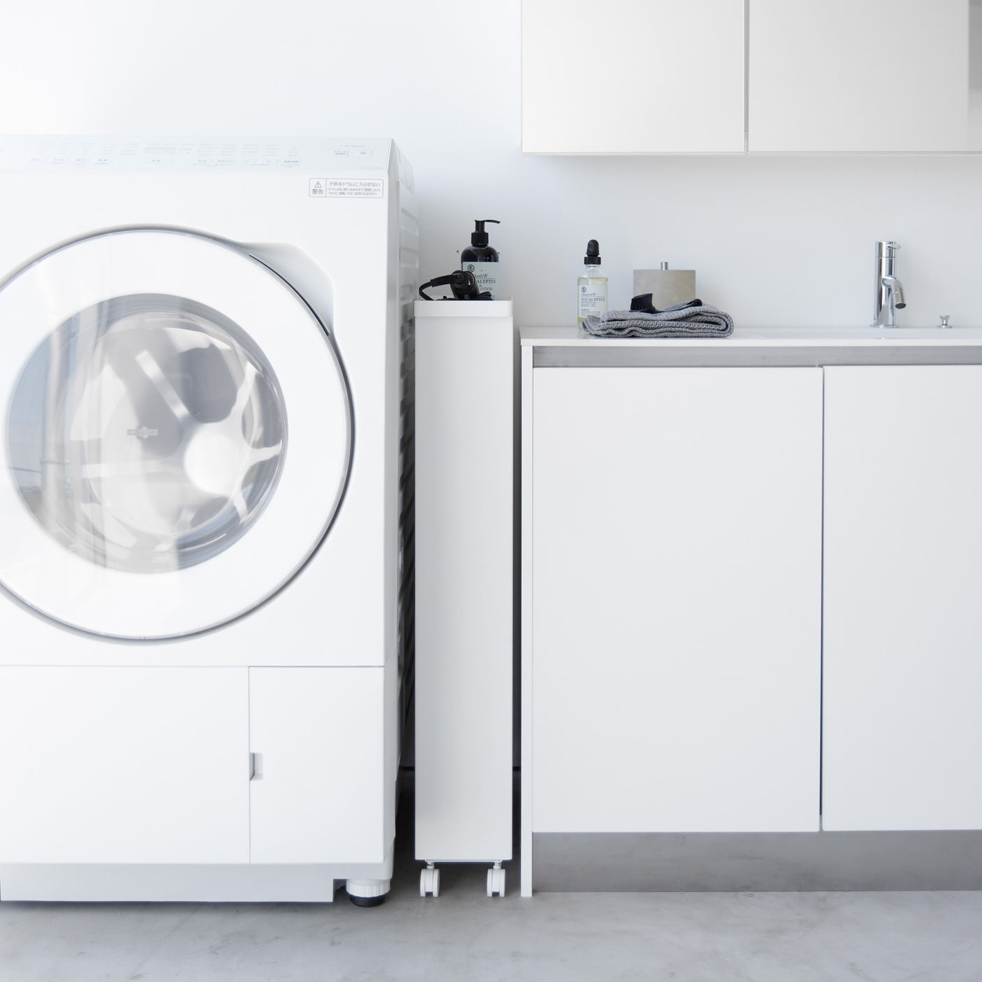 Smal hvit hyllevogn med oppbevaring av flasker og vaskemidler.