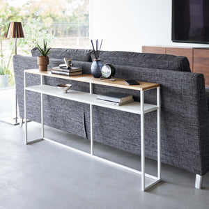 Konsollbord med hvit metallramme og treoverflate bak sofa.