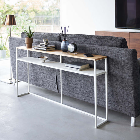 Konsollbord med hvit metallramme og treoverflate bak sofa.