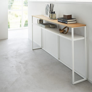 Hvit metallramme og trehylle på konsollbord ved vindu.